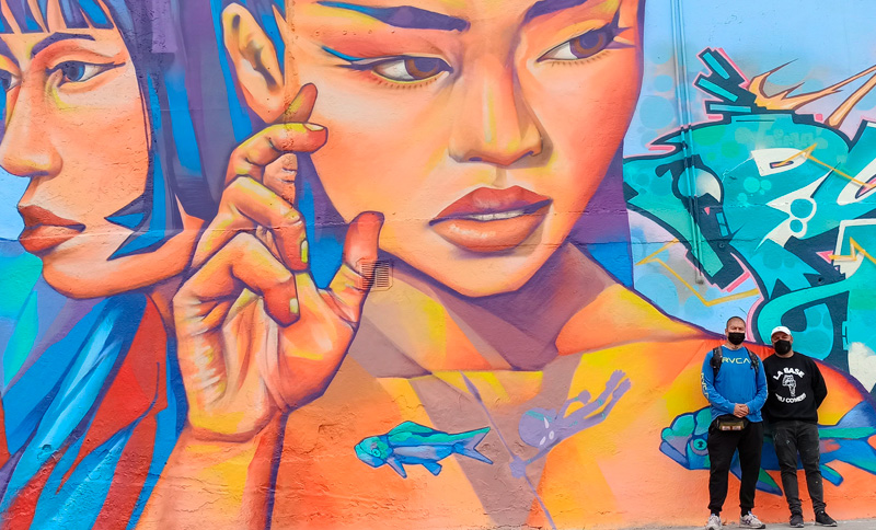 dos personas al lado de un murral con el diseño de dos mujeres