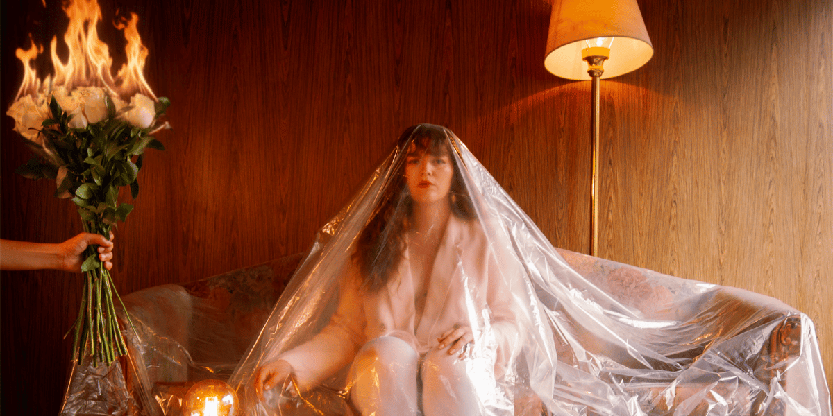 Fotografía de una mujer sentada en un sofa cubierta en plástico con unas rosas en llamas