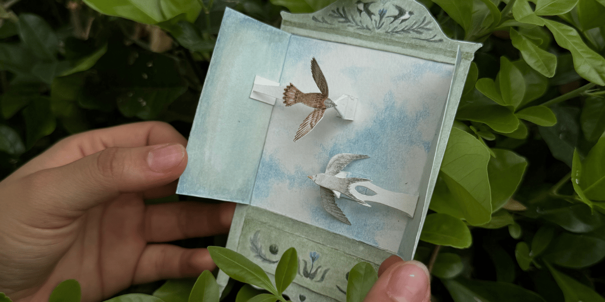 Fotografía de unas manos soteniendo una ventana de papel con aves