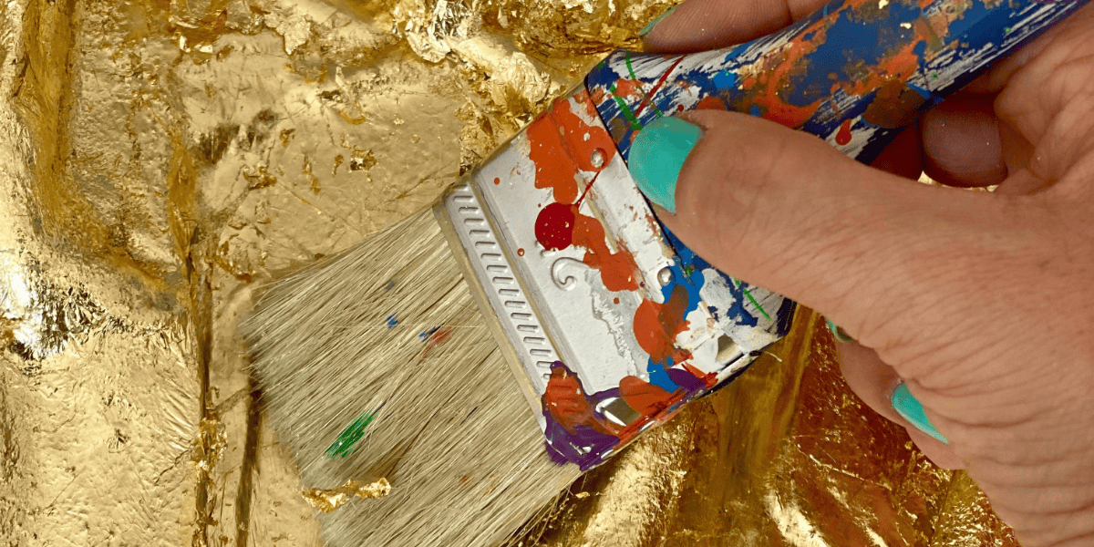 Fotografía de una mano con pincel pintando en dorado