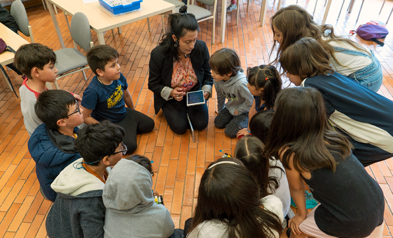 NIñas y niños reunidos escuchando a una persona adulta