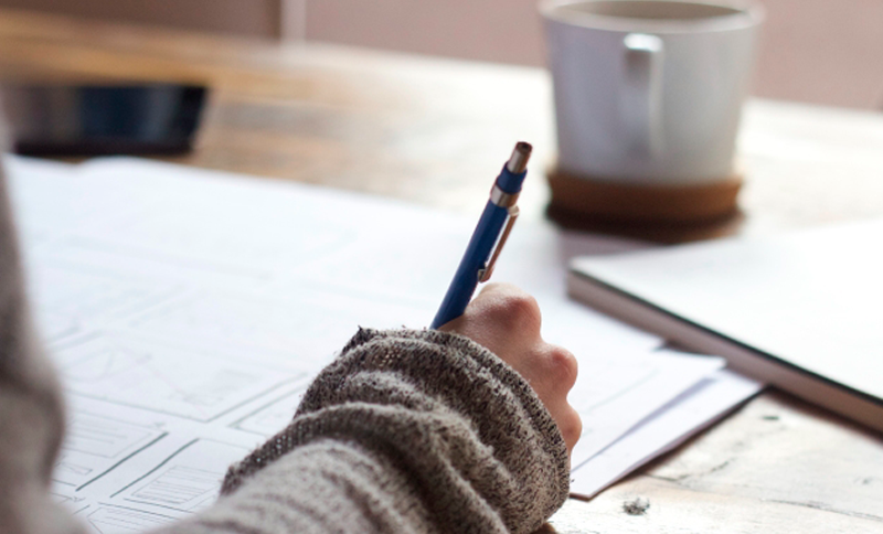 Mano escribiendo y de fondo una taza de café