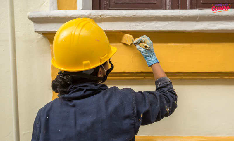 Mujer pintando una casa con pintura amarilla