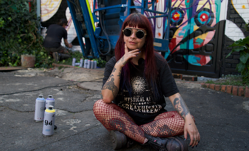 Mujer con gafas sentada en el pavimento mirando a la cámara