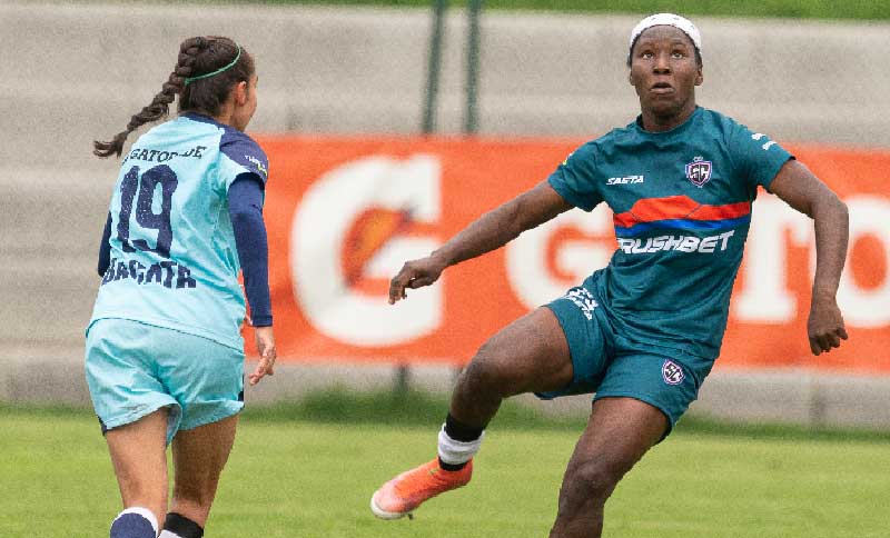 dos mujeres disputando una pelota en una cancha de fútbol