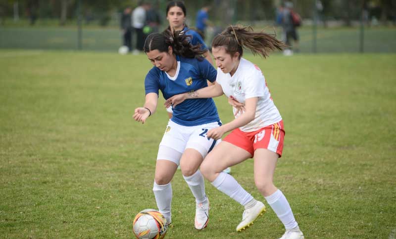 dos mujeres disputando una pelota en una cancha de fútbol