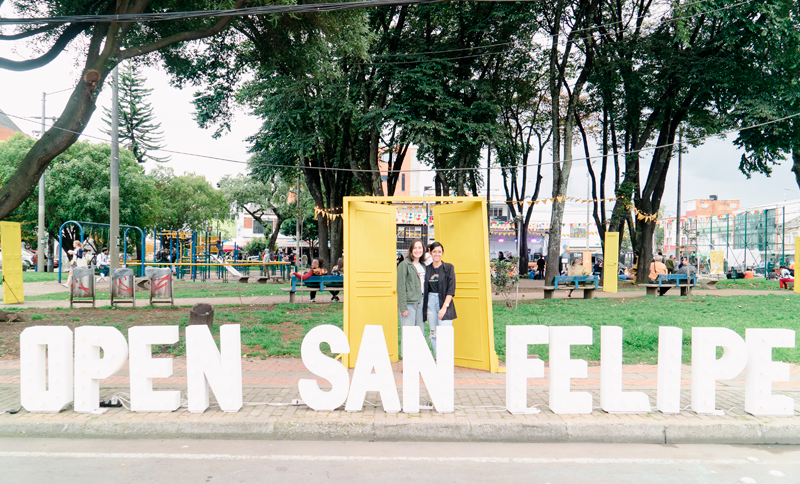 Dos mujeres en un parque y al lado de un letrero Open San felipe