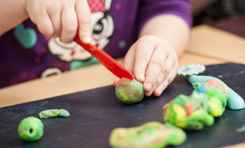 Manos de un niño cortando una plastilina