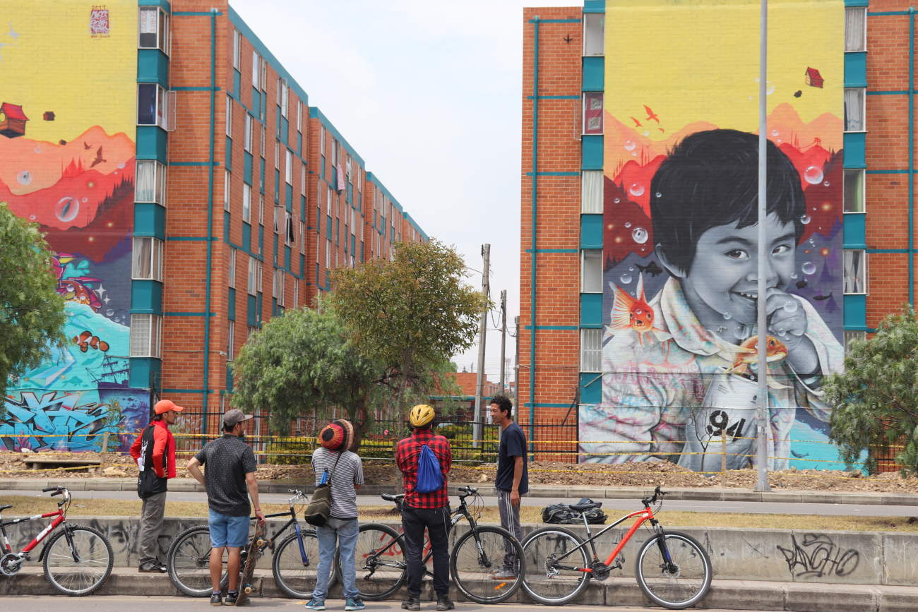 Mural de niño sonriendo sobre pared de conjunto residencial, personas observan