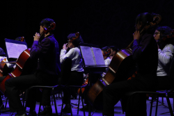 Niña de orquesta sinfónica ejecuta violonchelo