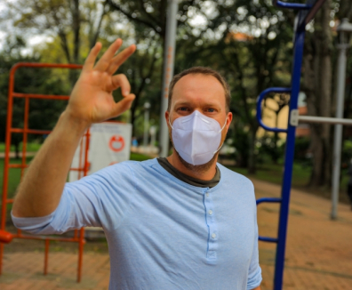 Hombre con tapabocas en un parque haciendo símbolo de OK con su mano