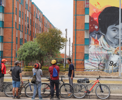 personas en bicicleta observando un grafiti en una fachada