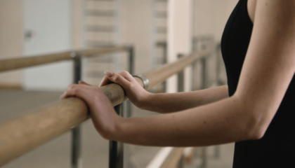 Mujer apoyada en barra de ballet.
