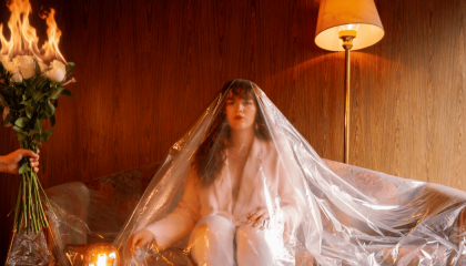 Fotografía de una mujer sentada en un sofa cubierta en plástico con unas rosas en llamas