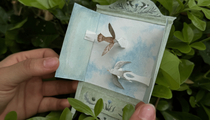 Fotografía de unas manos soteniendo una ventana de papel con aves