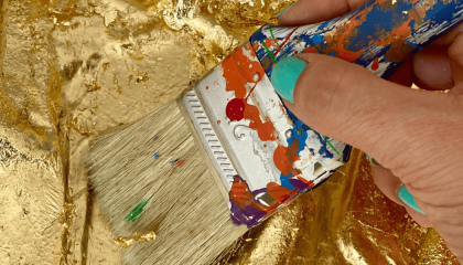 Fotografía de una mano con pincel pintando en dorado