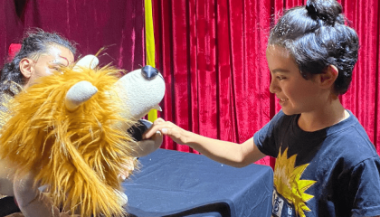 Fotografía de una obra de títeres con un león y un niño presente