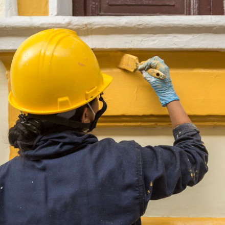 Mujer pintando una casa con pintura amarilla