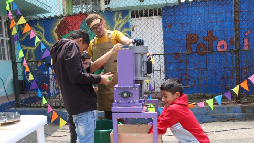 Niños con un profesor aprendiendo a el funcionamiento de una máquina de reciclaje