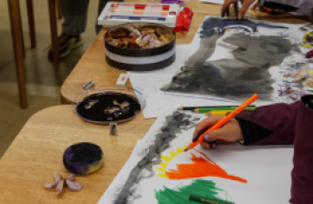 Fotografía de una mesa con implementos de dibujo y niños pintando